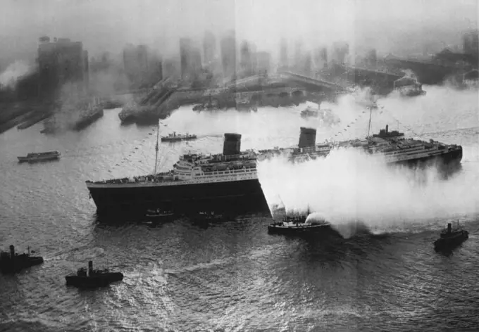 The Queen Completes Maiden Voyage As Luxury Liner -- Accompanied by water stream throwing fireboats, tugs and other craft as well as airplanes over head, the British luxury liner Queen Elizabeth, largest ship afloat, makes her way up New York harbour in the early morning haze today completing her first transatlantic voyage in passenger service. The Queen made many ocean voyages carrying troops during the war but this was her maiden trip since being refitted as the luxury liner she was originally intended to be. October 21, 1946. (Photo by AP Wirephoto).