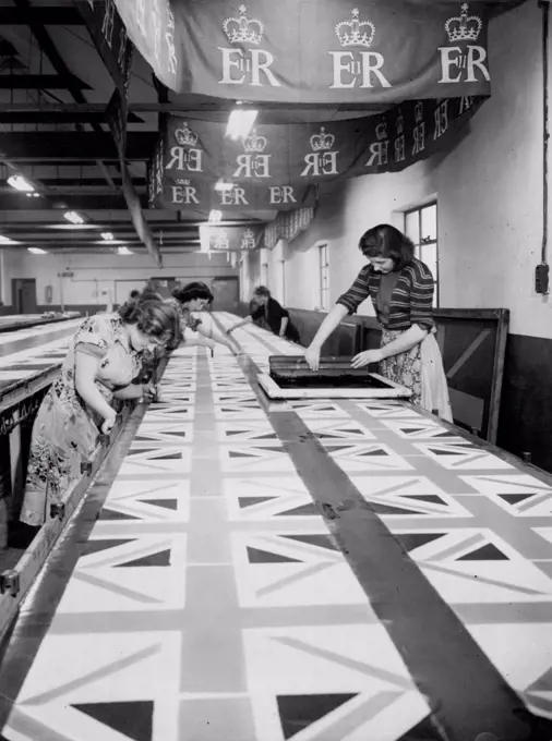 Flags By The Mile - For Coronation. Union Jacks that will give colour to Coronation day celebrations are finished by workers at a Rochford, Essex, factory. From the roof hang other banners, bearing the Crown and cipher. At work on the table are - left - Shipley Wellington (Rochford); and Brenda McGrath (Southend). At right of table - Jean Cushen (Eastwood) and Rita McGrath (Southend). January 12, 1953. (Photo by Reuterphoto).