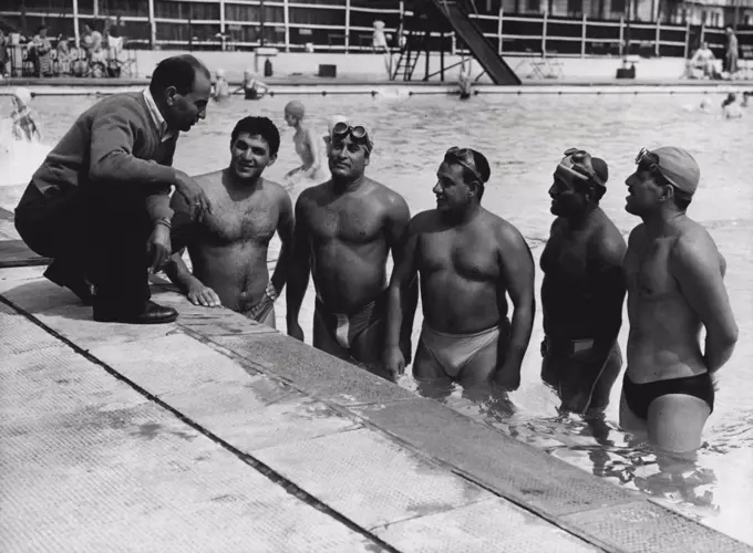 Channell Swimmers In Training - Amin Sabry, the trainer, stooping to have a few words with members of the Egyptian Channel swimming team, seen in training at the Open Air Sea Swimming Pool at Folkestone. They are (left to right): Fouad Bayoumi: Helmy Ei, Maraghy: Nazik Reiad: Bakr Soliman and Fouad El Ghazali. With the opening once again of the Channel swimming season, ten brawny Egyptian swimmers, with their trainer have arrived at Folkestone, where they are now in striot training. In addition to swimming the channel, they hope to swim from Capri to Naples and from Nante to St. Nazaire this summer. August 9, 1954. (Photo by Fox Photos).