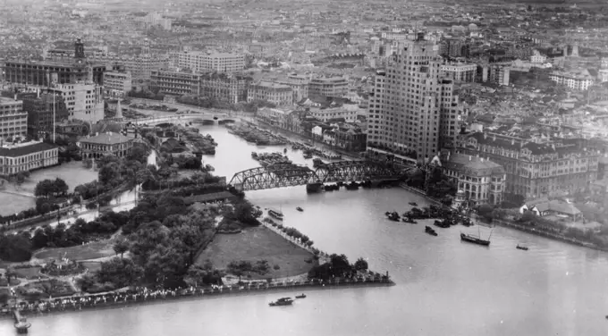 Shanghai.On the right bank of Soochow Creek is seen the Astor Hotel, on the left bank behind the park is the old British Consulate. Many people are seen along waters edge viewing Navy TBM overhead. October 15, 1945. (Photo by Official U.S. Navy Photo).