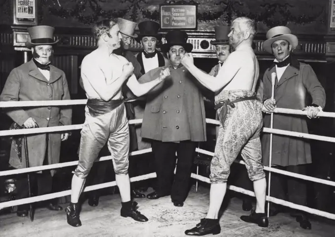 Prize-Fighting as it was in 1960 and Boxing as it is Expected to be in 1980 -  Pat O'keefe (right) with Bill Knight, as the prize-fighters of 1960 with the referee and seconds. A novel boxing set was staged at the "Ring" Blackfriers Road, when a tournament was held for charity.Pat O'Keefe, the old middle-weight champion, with the aid of a sparring partner, gave a representation of prize-fight in 1860.The pair fought in the clothes and under the rules which were the custom in that year.Late O'Keefo returned with his partner and depicted boxing as he expects is to be in 1960. January 16, 1933. (Photo by Central News).