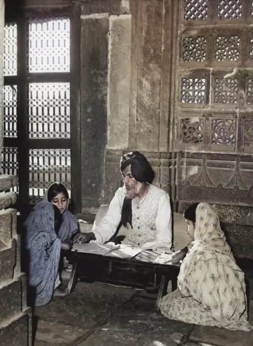 Shrine Of Learning - In the Quiet of an Old Muslim Shrine, a teacher gives lessons on the Koran to young Muslim girls. This picture was taken at Ahmedabad, Capital of Gujarat. It is one of the shrines of the old Modul Emperors, now used primarily as religious schools. Both teacher and pupil have to sit on the ground with their books on special racks. September 01, 1953. (Photo by Paul Popper, Paul Popper Ltd.).