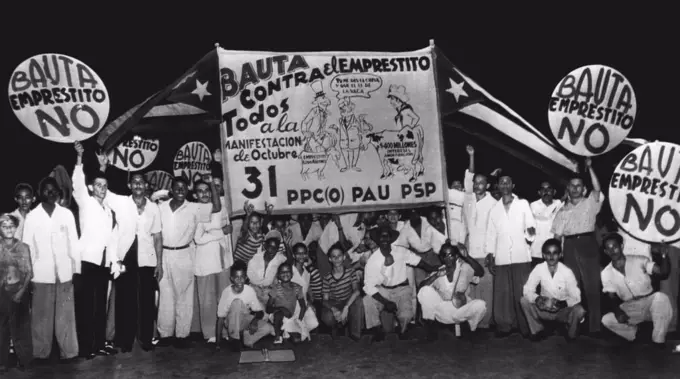 Demonstrate Against World Bank Loan To Cuba -- A delegation of Cubans from Bauta, near Havana, display signs they carried in the Oct. 31 demonstration in Havana against a proposed World Bank loan to Cuba. Sign depicts Uncle Sam leading a goat labeled "$200,000,000 Loan" while a typical Cuban leads a cow labeled to represent the $400,000,000 the protesters say Cuba will pay in amortization of such a loan. The center figure is Cuban President Carlos Prio Socarras telling Uncle Sam "You give me the goat and I'll give you the cow" -- which the demonstrators regard as a poor exchange. November 02, 1949. (Photo by AP Wirephoto).