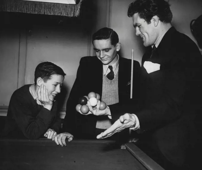 A Snooker Hand! -- Freddie Mills, the boxer, was watching play at Burroughes today. He showed Carney and Smith (leaning on table) a trick they didn't know - he can hold 12 snooker balls in one hand!The semi-finals of the boys billiards championship were played off today at Burroughs Hall, London, Jack Carney, aged 15, of Ponterdawe, won his match to enter the final Colin Smith, of Crook, Durham, was expected to win the other match. January 2, 1948. (Photo by Fox).
