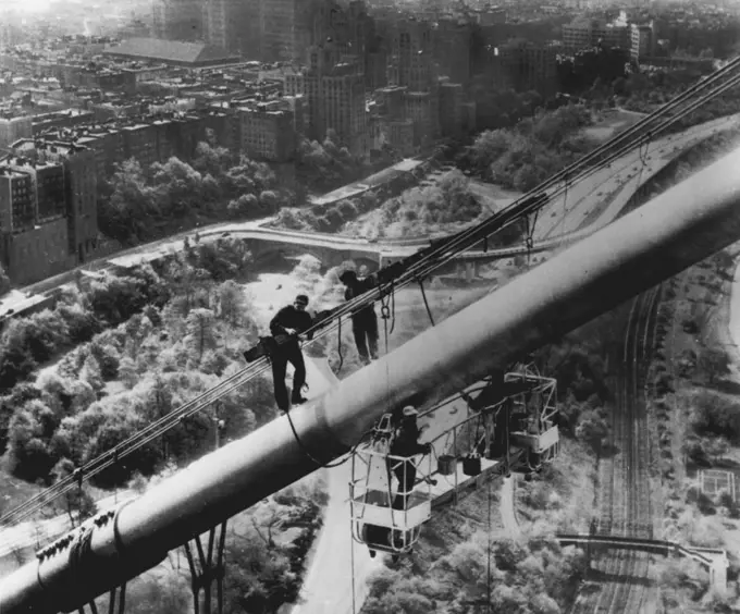 Spring Cleaning -- Painters using an electrically operated scaffold, called "spider staging," work on a cable high above the Manhattan side of the George Washington Bridge as part of a force of 50 carefully picked workmen who yesterday started a two-year painting job. The project will cost $150,000, including $35,000 for 11,000 gallons of paint. In background are apartment buildings along Riverside Drive, and below the workmen are the West Side Highway and the New York Central Railroad tracks. May 08, 1954. (Photo by AP Wirephoto).