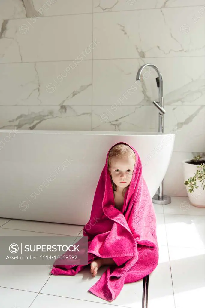 little girl sitting on the floor in the bath in a pink towel
