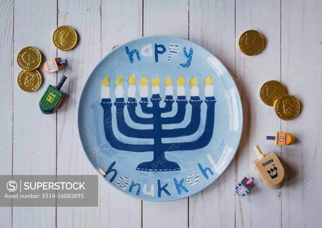 Happy Hanukkah plate, dreidels and chocolate coins on white wood.