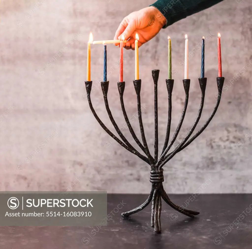 Cropped image of a hand lighting candles on menorah for Hanukkah.
