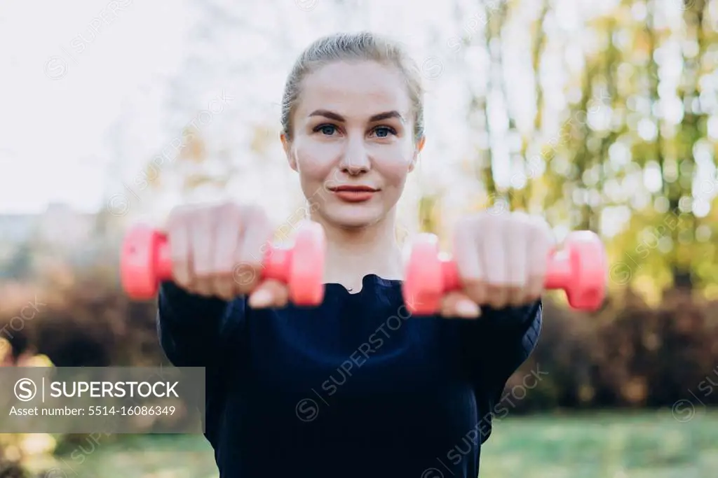 Beautiful young girl holding dumbbells stretched out in front of her.