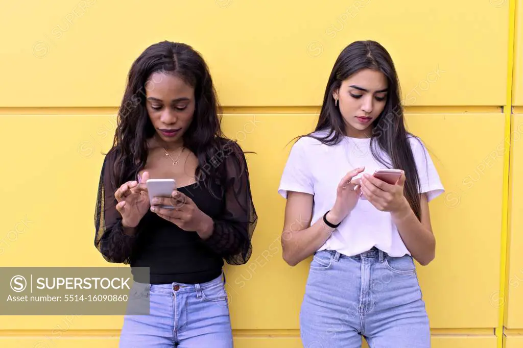 two friends of different races chatting on their smartphones
