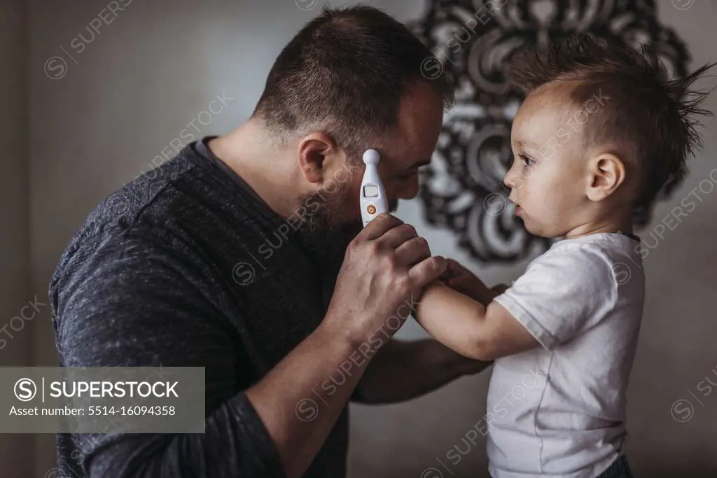 One year old boy taking father's temperature at home during isolation