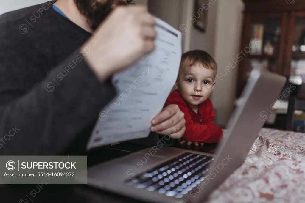 Close up of young son looking at dads computer while he works at home
