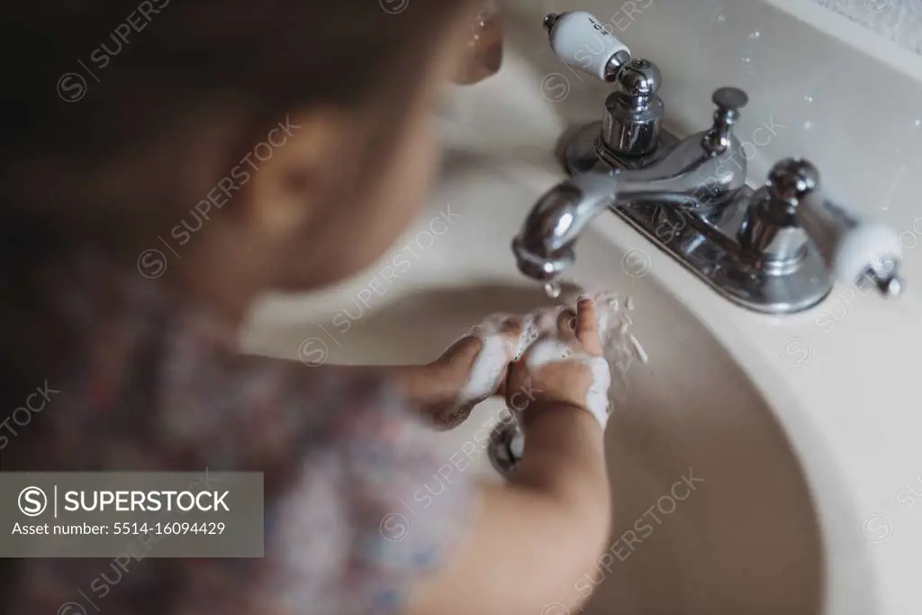 Young preschool aged girl washing hands in sink with soap