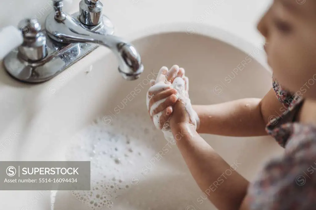High angle view of young girl washing hands in sink with soap
