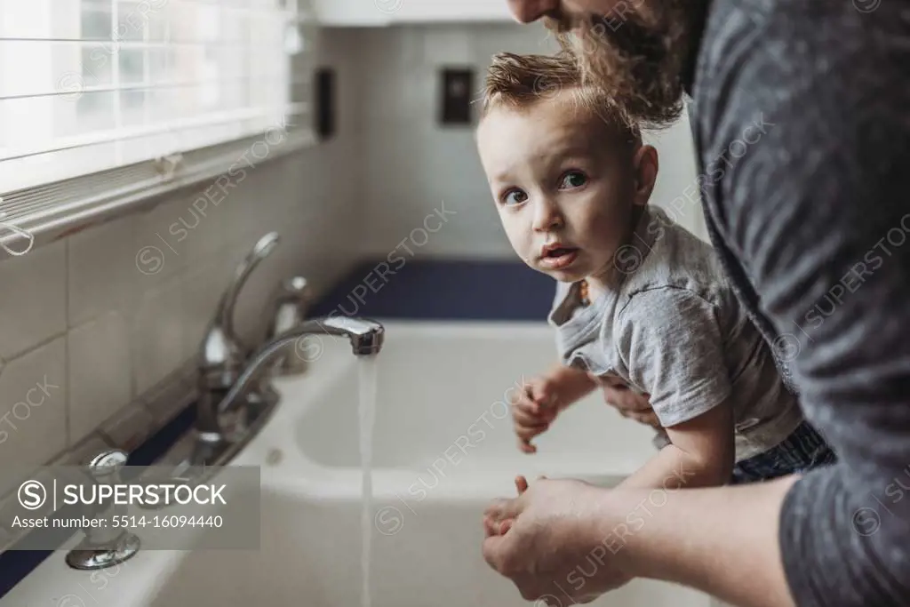 Side view of young boy having hands washed in sink by dad