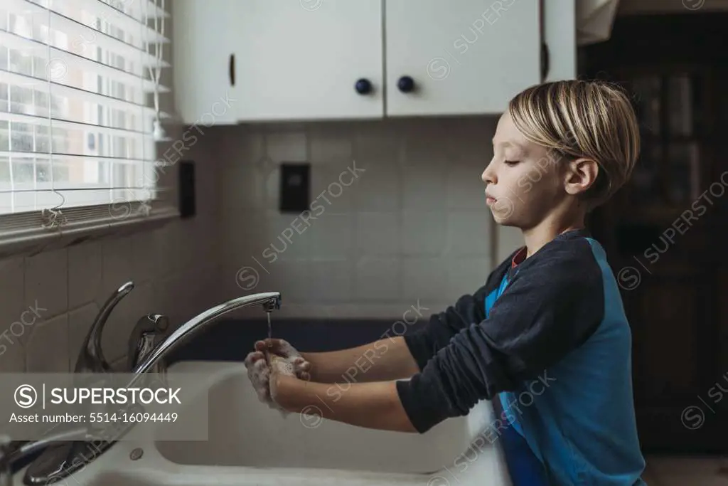 Side view of school aged boy wasking hands at sink in kitchen