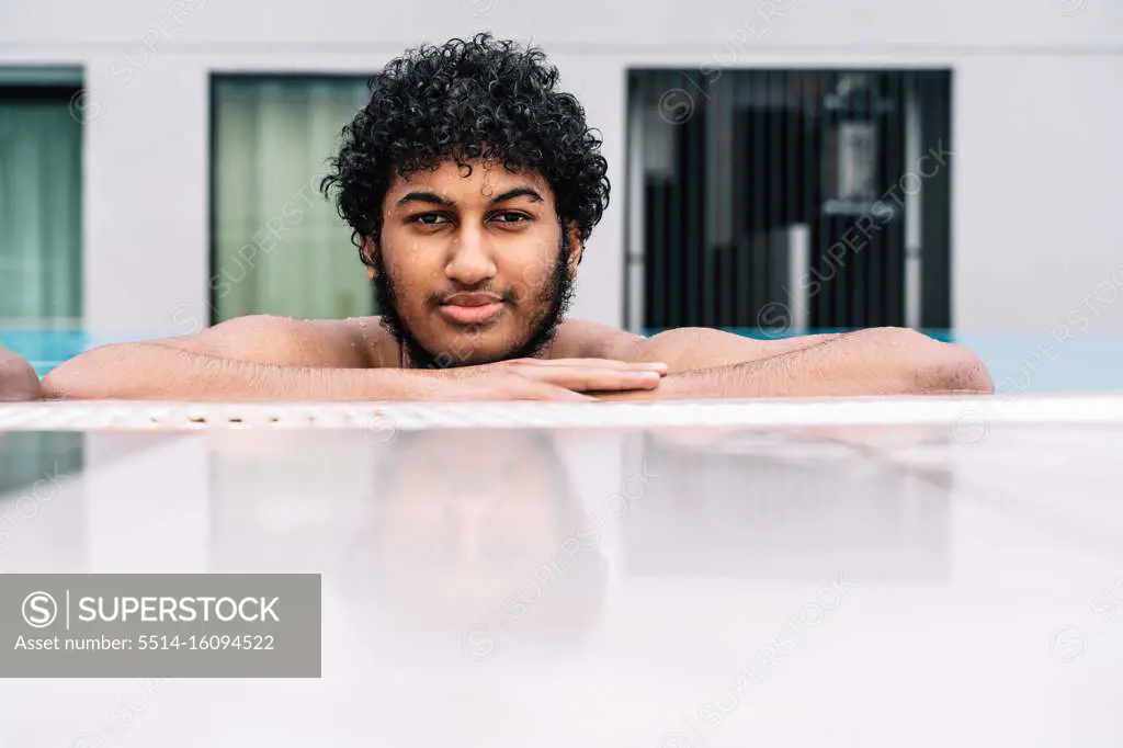 Young Arabian man with curly hair leaning on the edge of a pool