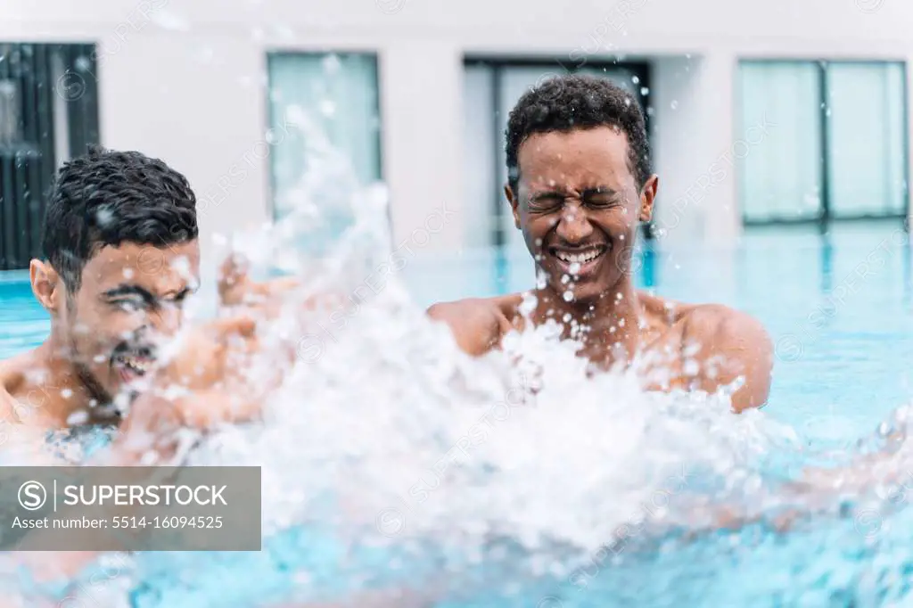Man smiling with his eyes closed as he splashes around playing with his friends in the water of a pool