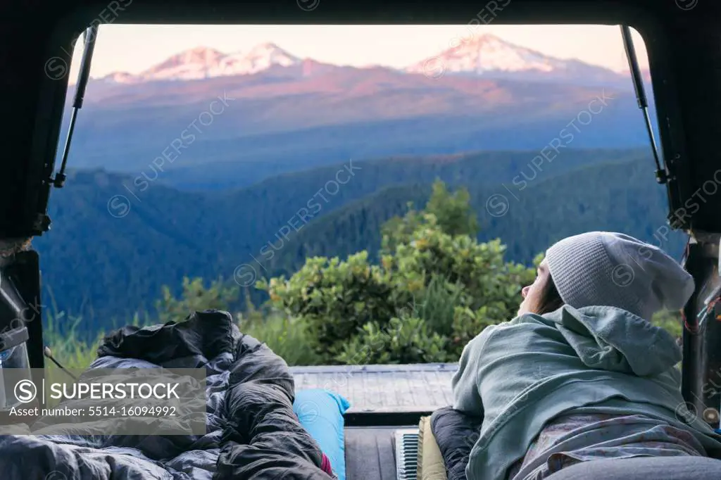 Young woman laying in back of truck looking out at mountains