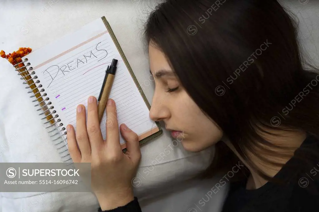 Notebook with the word Dreams written, next to a sleeping woman.