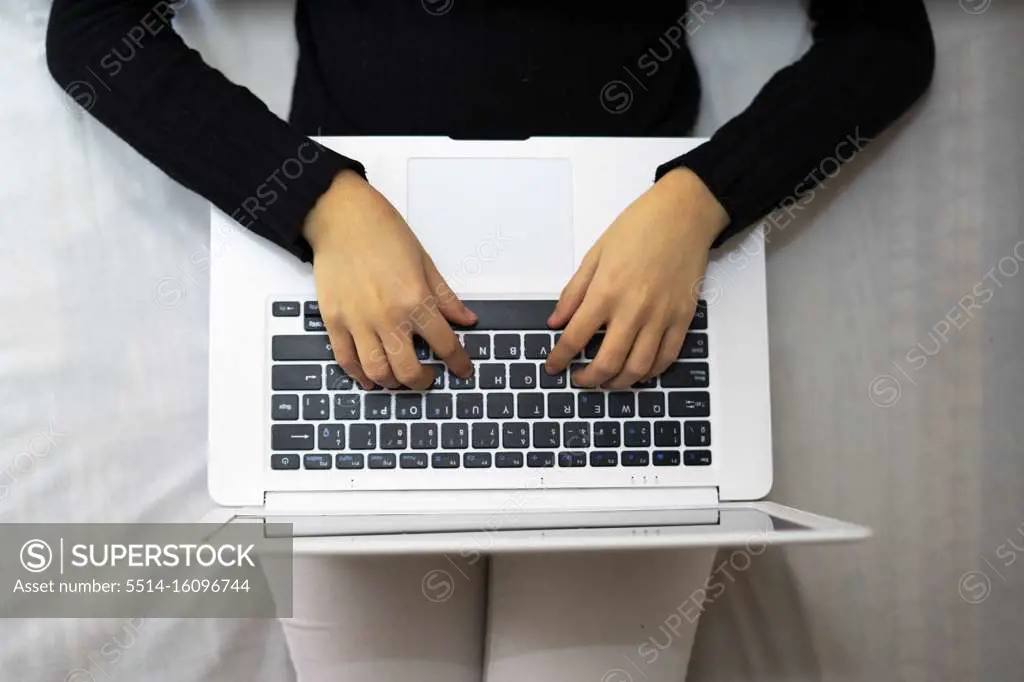 Top view of a woman using and working on a laptop in bed.