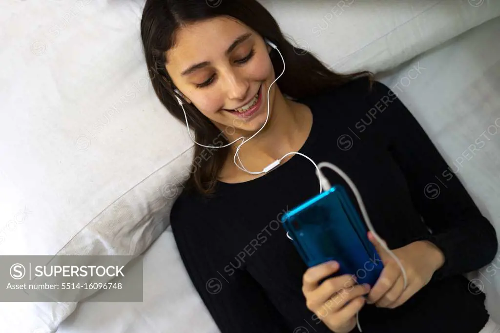 Woman listening to music on a white bed.