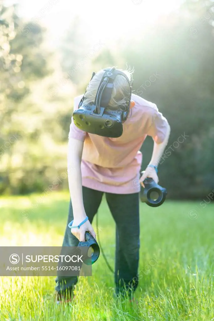 Tween playing virtual reality game in green field with VR goggles on