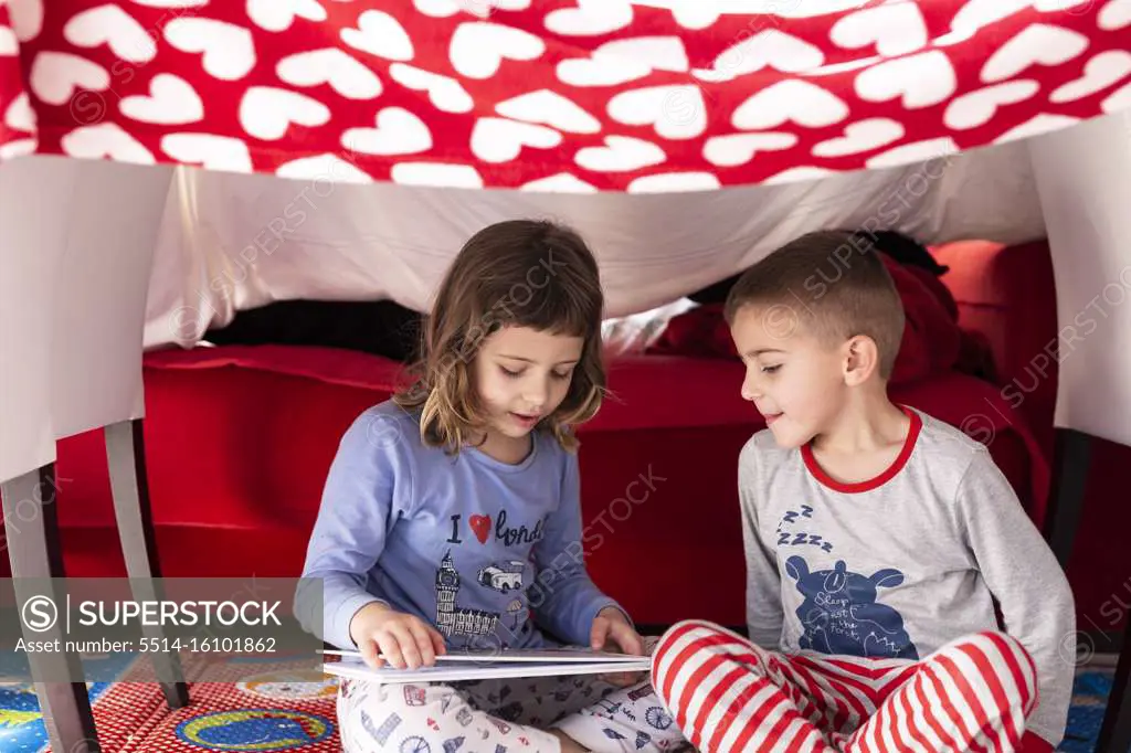 Girl reads a story to her brother at home during the coronavirus quarantine