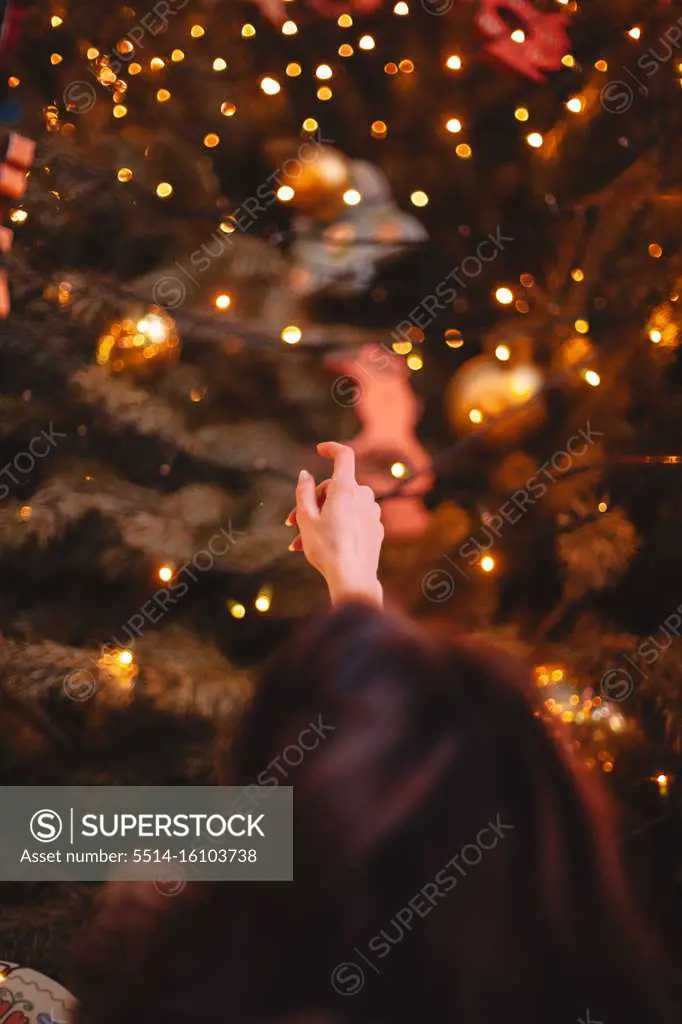 Rear view of teenage girl reaching to Christmas tree making a wish