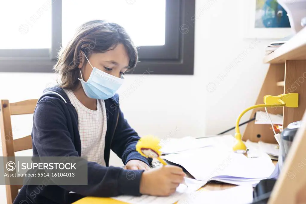 Young spanish boy doing homework while using a mask