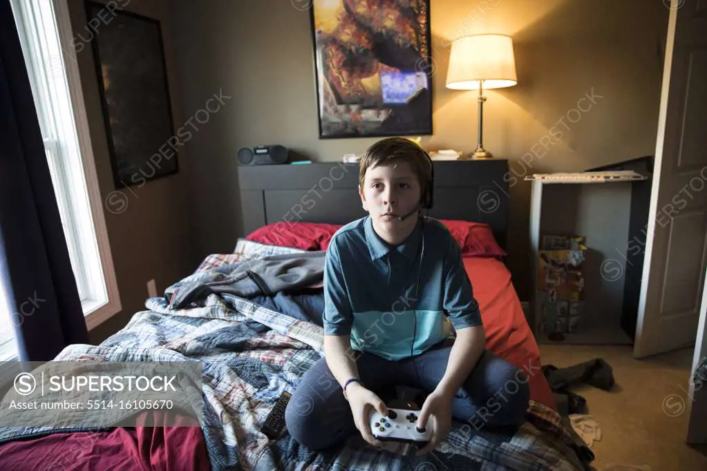 High View of Teen Boy Gaming While Wearing Headset, Sitting on Bed