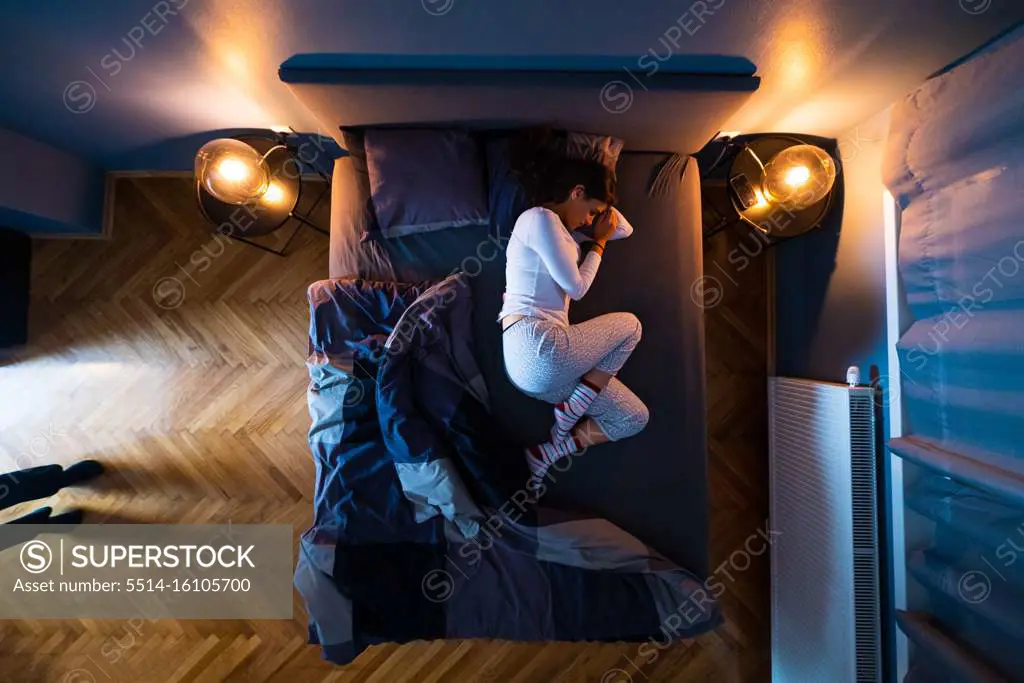 Image from above of vulnerable young girl at her bed during the 