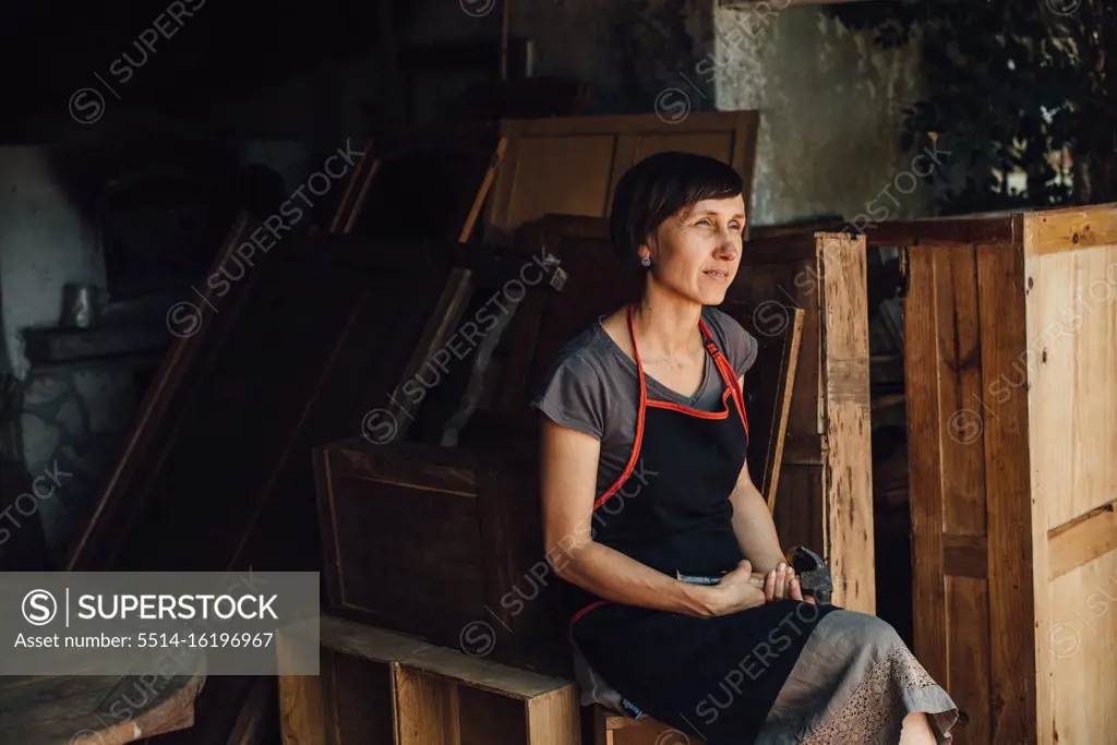 Thoughtful woman sitting in workshop surrounded by old wooden things
