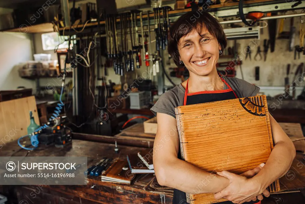 Female artist holding her wooden art work and smiling in a workshop
