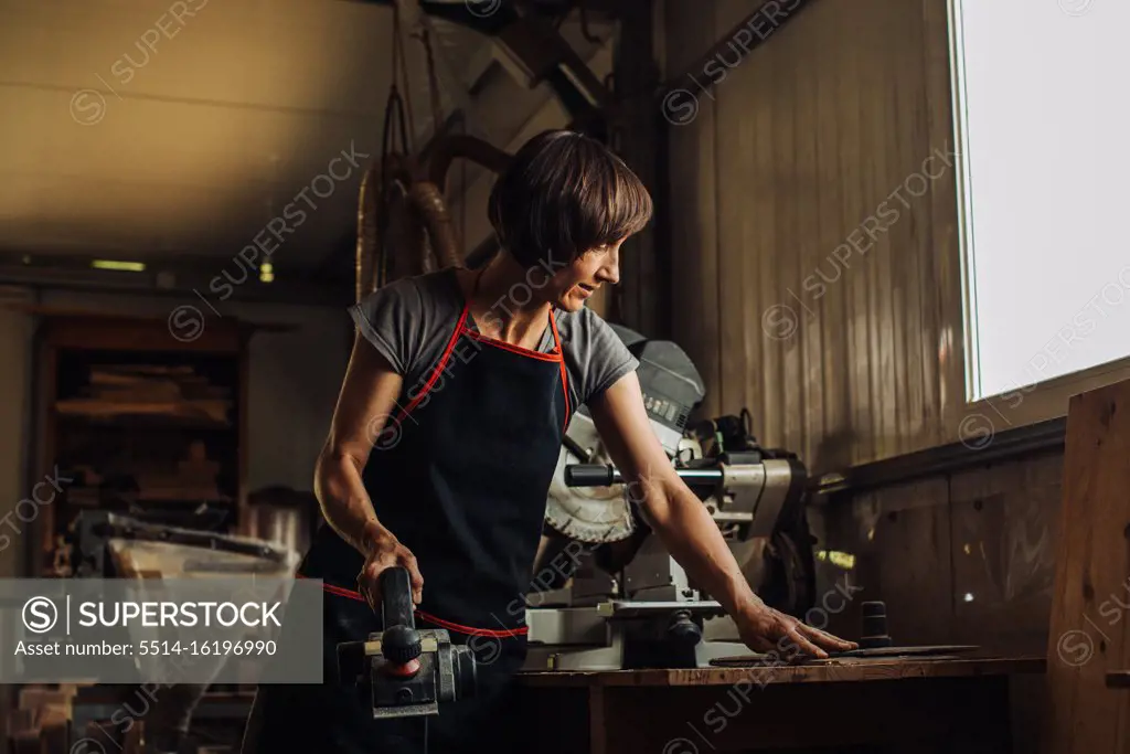 Middle aged woman with power planer in a wood shop