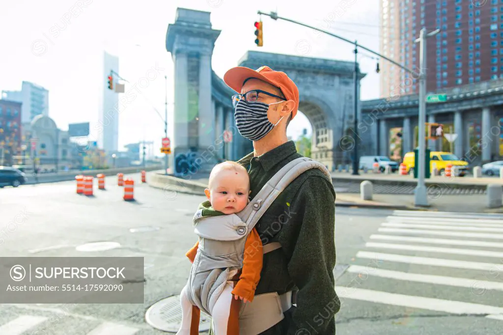Father carrying daughter in baby carrier while walking on street in city during coronavirus pandemic