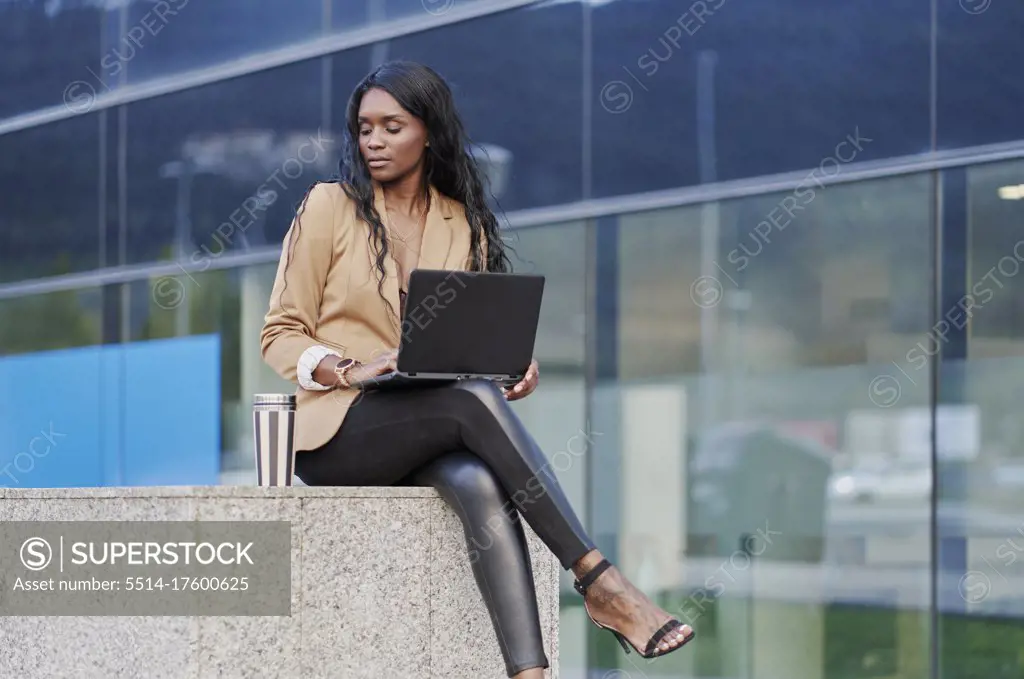 Portrait of a black executive woman sitting in a brown suit talking on the phone and holding a laptop
