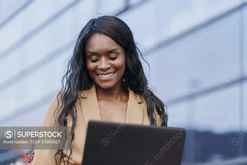 Portrait of black woman wearing a brown suit working on her laptop in the street