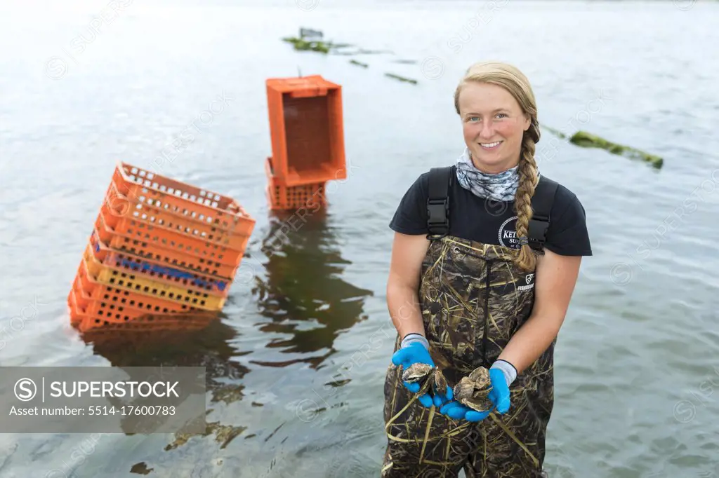 female shellfish farmer in water holding oysters in hands