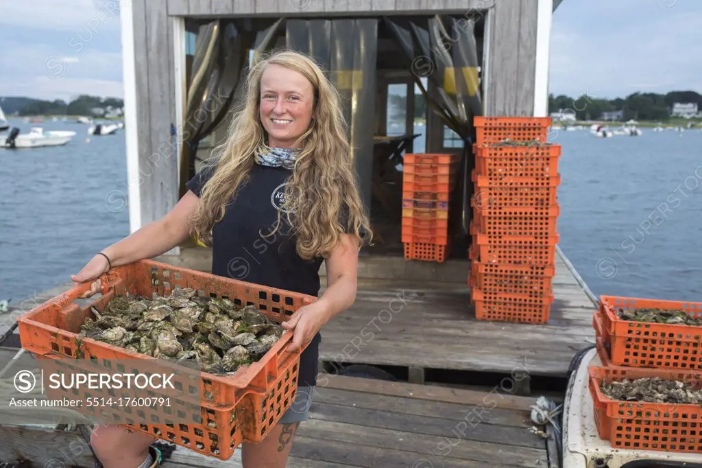 Female shellfish farmer carrying crate of oysters