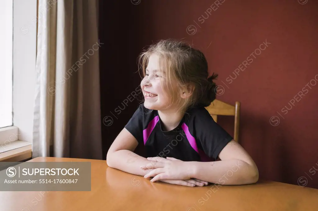 Young girl sitting inside at the dining room table looking outside
