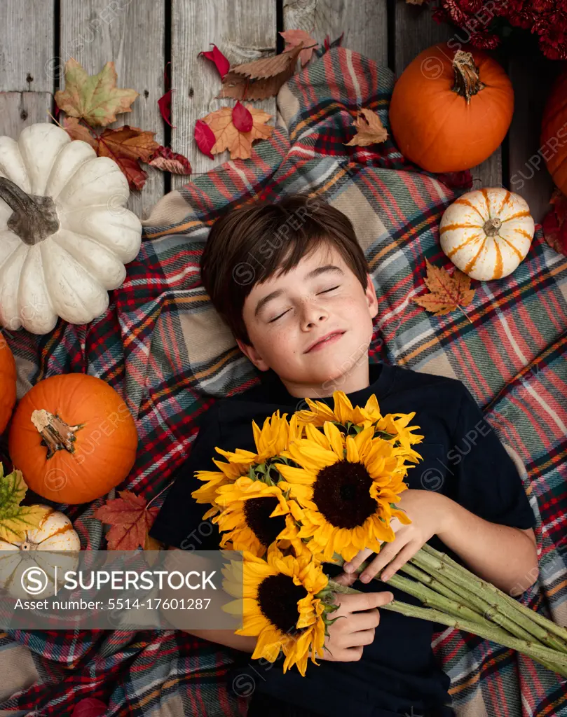 Overhead view of boy holding sunflowers surrounded by fall items.
