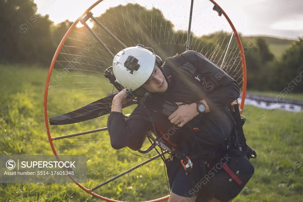 Young man, with the Powered Paragliding engine in his shoulders, gets ready to fly at sunset.