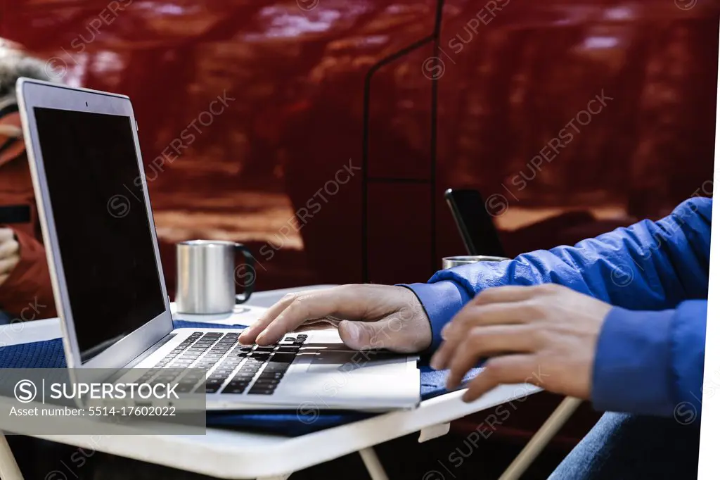 Close up young man working on laptop near car in forest - Stock Photo
