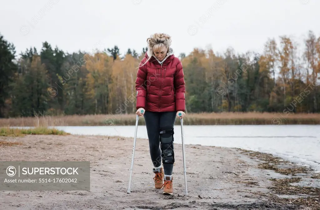injured woman walking with crutches on the beach looking thoughtful
