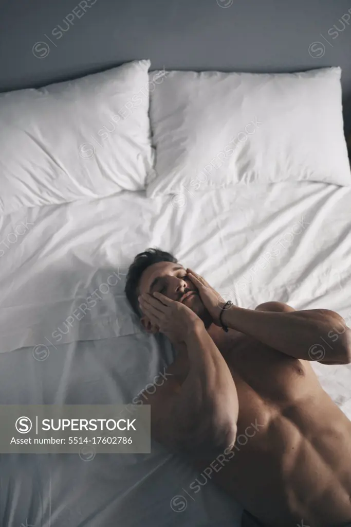 Portrait of a naked boy lying in bed crying