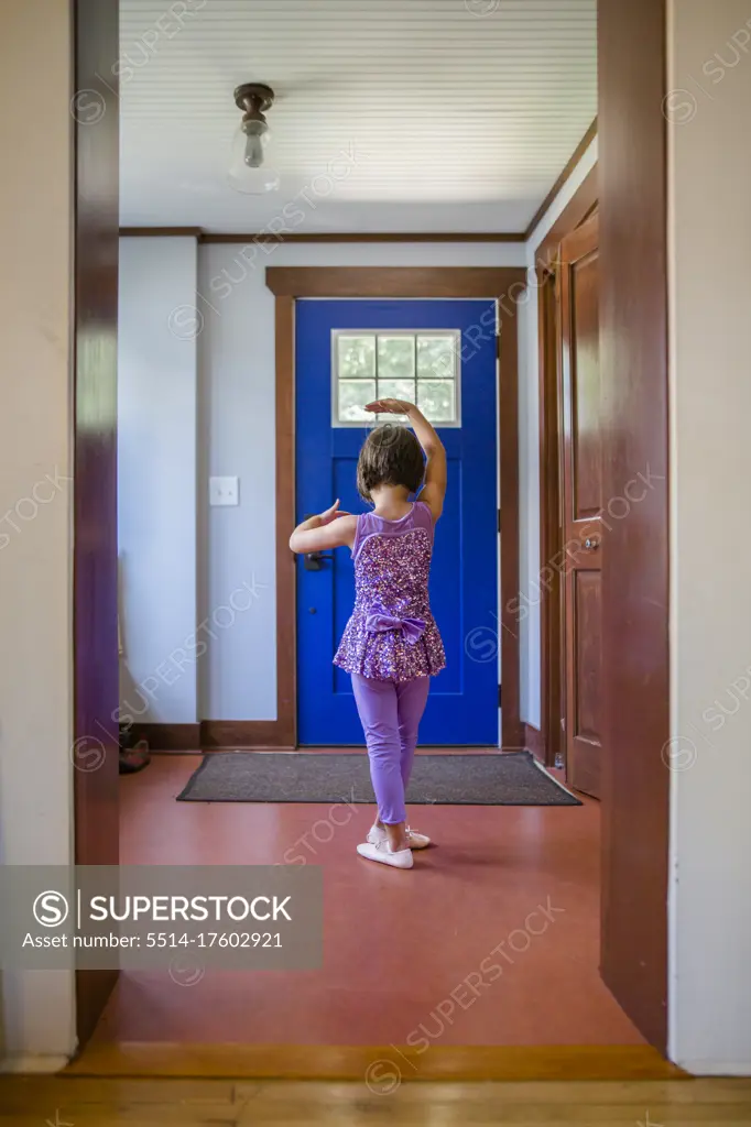 A small girl in a sparkly ballet costume dances in her front entryway