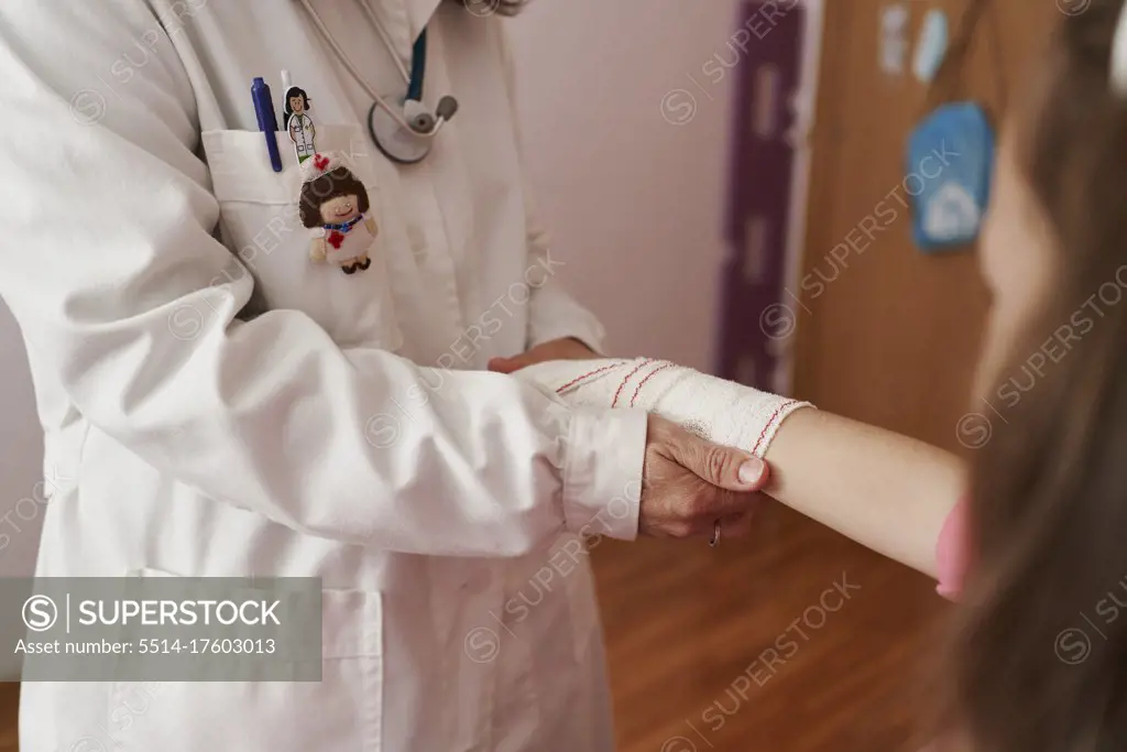 side view of a female doctor bandaging the arm of a little girl in her room. Home doctor concept