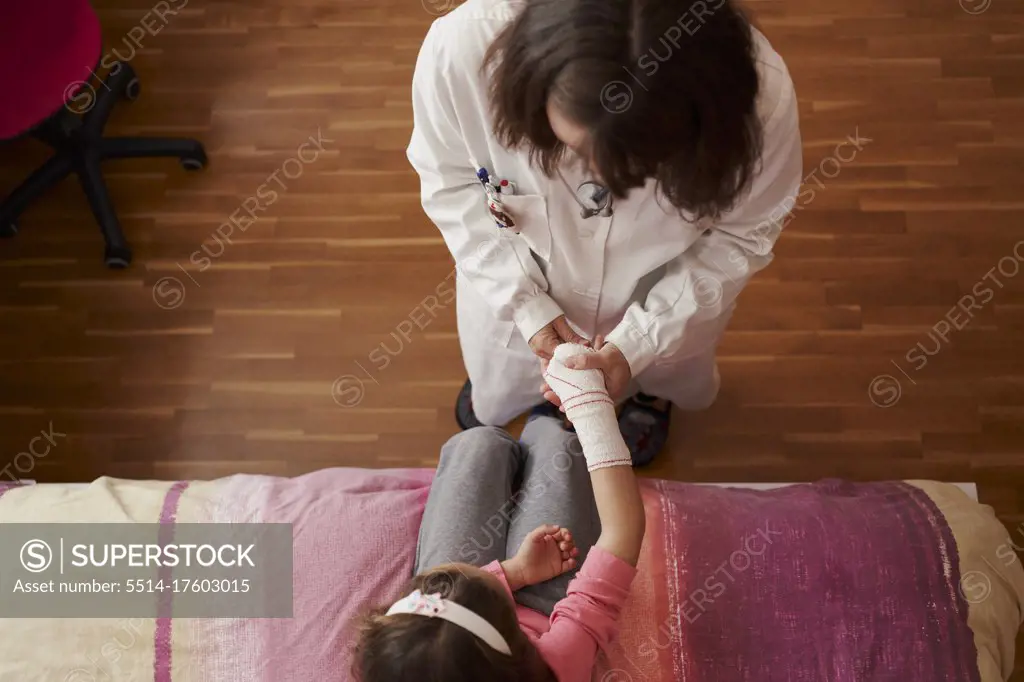 Top view of female doctor bandaging the arm of a little girl in her room. Home doctor concept