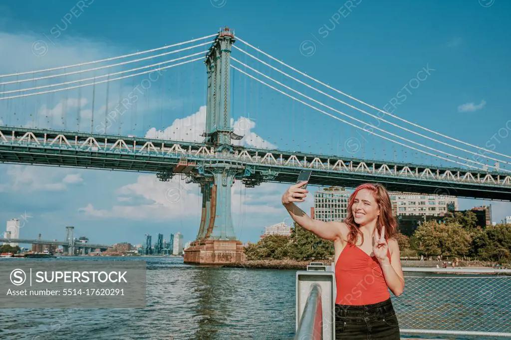 Young woman standing by river taking selfie.